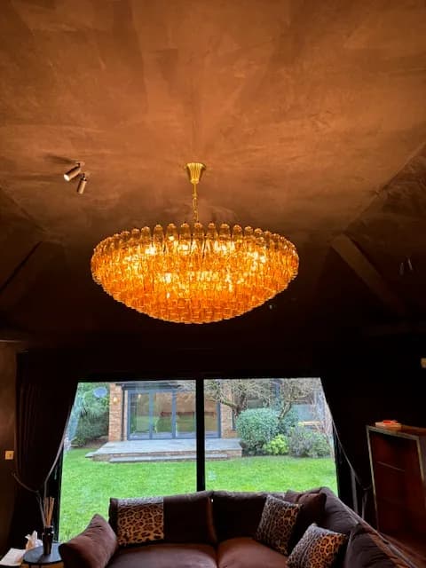Large amber glass chandelier hung from the vaulted ceiling of a garden room looking out over the lawn